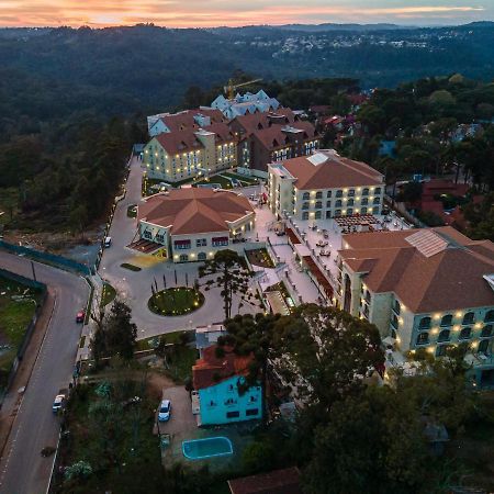 Hotel Buona Vitta Gramado by Gramado Parks Esterno foto The photo shows an aerial view of a hotel complex set in a hilly, wooded area. The buildings feature a mix of architectural styles with several structures, including a central round pavilion. Surrounding the buildings are well-maintained gardens and 