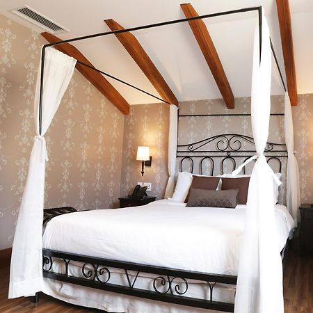 Hotel Buona Vitta Gramado by Gramado Parks Esterno foto The photo shows a beautifully designed bedroom featuring a four-poster bed with a metal frame and flowing white curtains. The bed is adorned with white bedding and brown decorative pillows. The room has wooden beams on the ceiling and is decorated wi