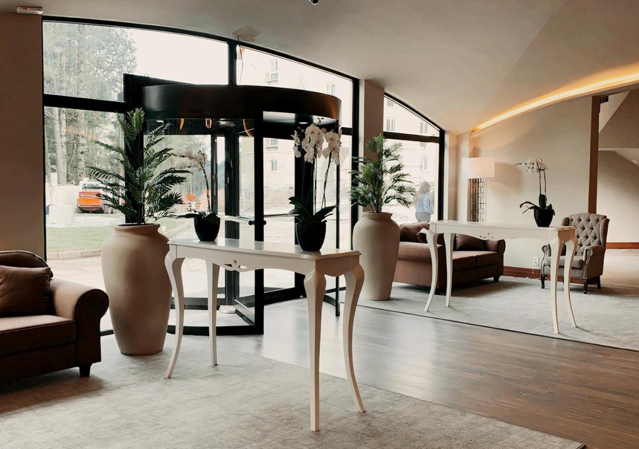 Hotel Buona Vitta Gramado by Gramado Parks Esterno foto The photo displays an elegant interior space, likely a hotel or a high-end lobby. In the foreground, there is a stylish table with a curved design, positioned near large glass doors leading outside. Flanking the table are two large planters with lush