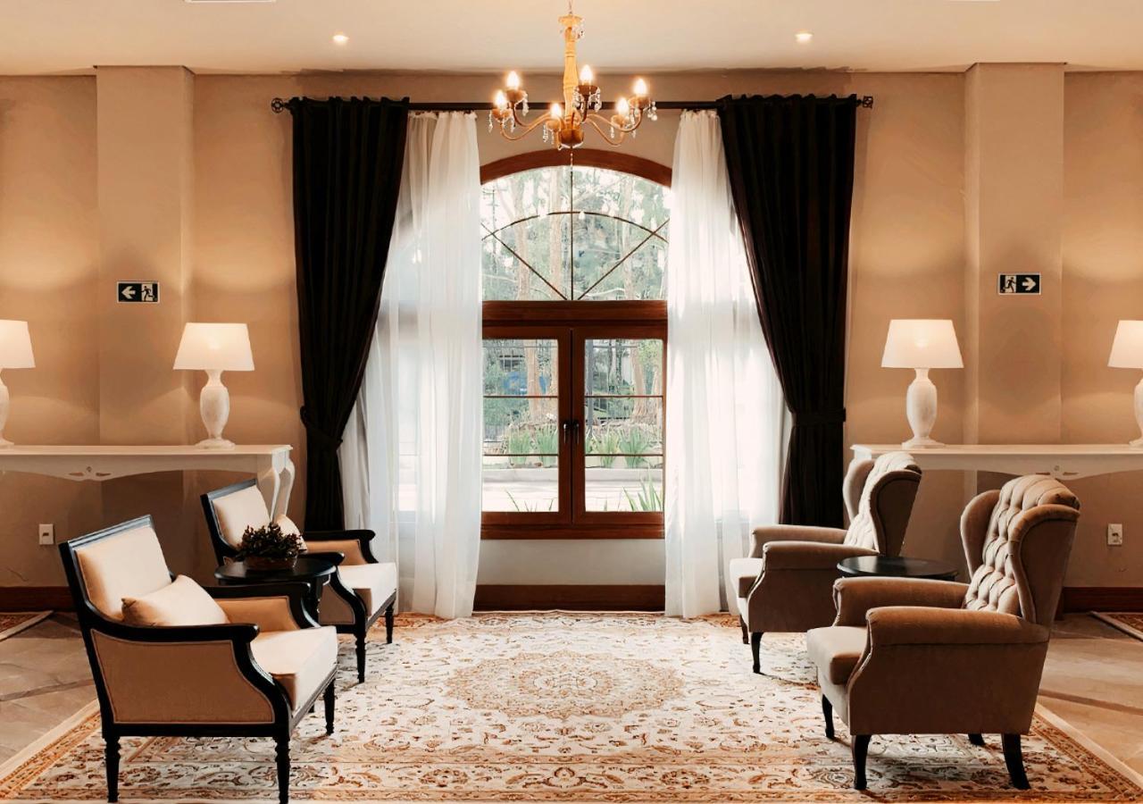 Hotel Buona Vitta Gramado by Gramado Parks Esterno foto The photo shows an elegantly styled living room. There are two armchairs and a sofa arranged comfortably around an intricate area rug. Large windows are adorned with sheer white curtains and dark curtains, allowing natural light to fill the space. A 