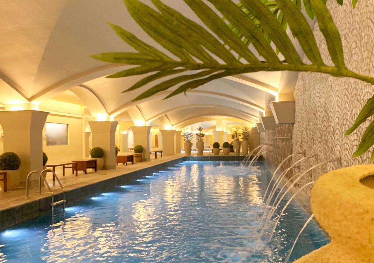 Hotel Buona Vitta Gramado by Gramado Parks Esterno foto The photo shows an indoor swimming pool with a serene and elegant atmosphere. The pool has a calm blue water surface, illuminated by soft lights along its edges. The architectural design features arches in the ceiling, creating an open and spacious f