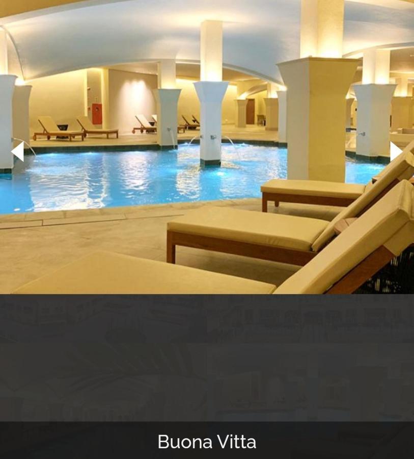 Hotel Buona Vitta Gramado by Gramado Parks Esterno foto The photo shows a tranquil indoor pool area, featuring a large swimming pool with clear blue water. Surrounding the pool are several lounge chairs made of light-colored wood, positioned for relaxation. The space is well-lit, with soft lighting highli