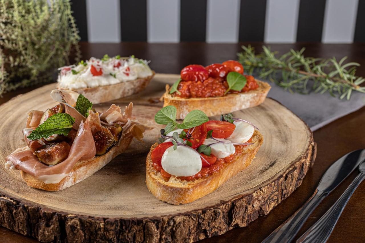 Hotel Buona Vitta Gramado by Gramado Parks Esterno foto The photo displays a wooden serving platter featuring four different types of bruschetta. Each piece of bruschetta is topped with various ingredients:

1. The top left has a creamy spread, possibly cheese or ricotta, garnished with fresh herbs and sm