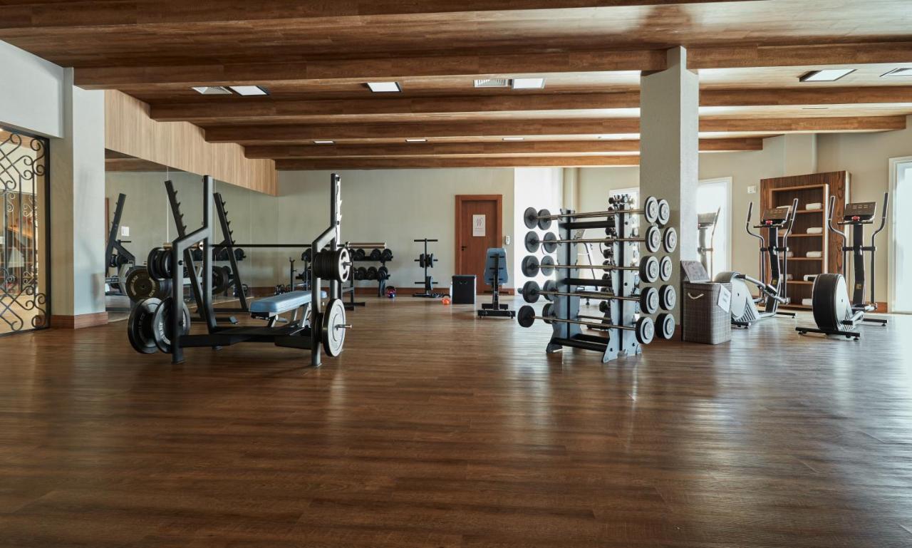 Hotel Buona Vitta Gramado by Gramado Parks Esterno foto The photo shows a spacious gym with a wooden floor and wooden ceiling beams. Various pieces of gym equipment are visible, including weight benches and racks with weights. On one side, there are free weights organized on a rack, while other equipment 