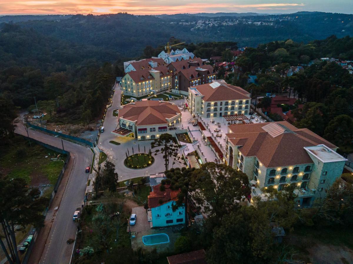 Hotel Buona Vitta Gramado by Gramado Parks Esterno foto The photo shows an aerial view of a hotel complex set in a hilly, wooded area. The buildings feature a mix of architectural styles with several structures, including a central round pavilion. Surrounding the buildings are well-maintained gardens and 