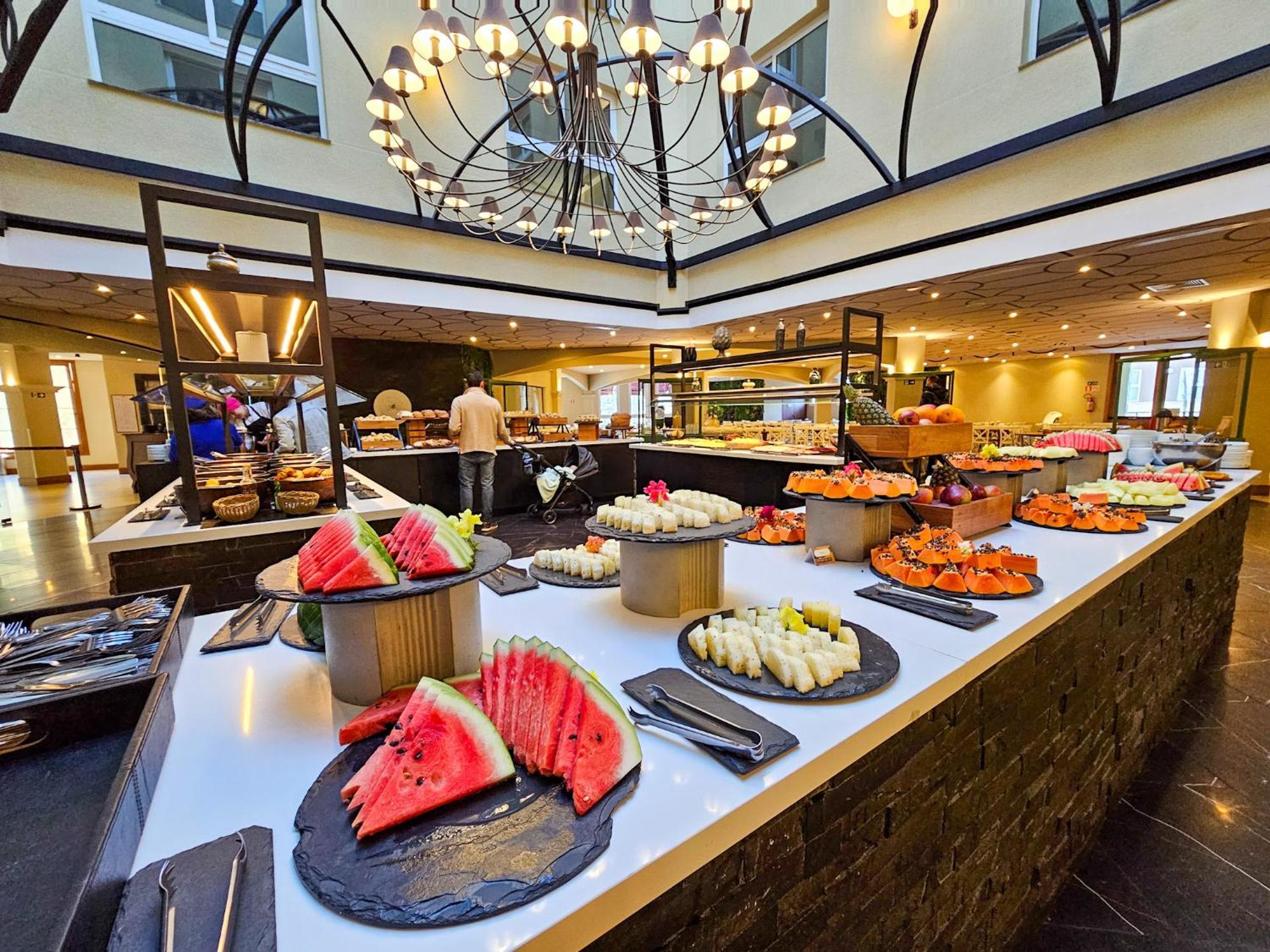 Hotel Buona Vitta Gramado by Gramado Parks Esterno foto The photo depicts a lavish buffet setup in a dining area. In the foreground, there are several platters featuring an assortment of colorful food items, primarily fruits like watermelon and various types of sushi or rolls. The buffet table is elegantl