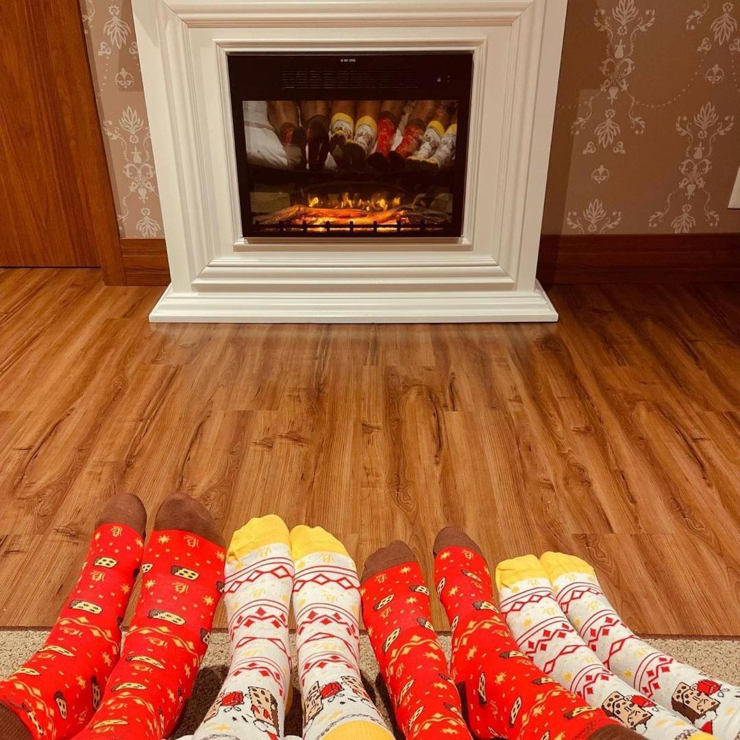 Hotel Buona Vitta Gramado by Gramado Parks Esterno foto The photo shows a cozy indoor setting with a warm fireplace. In the foreground, several pairs of feet are displayed, each wearing brightly colored socks with various patterns. The socks include red, yellow, and white designs, contributing to a cheerf