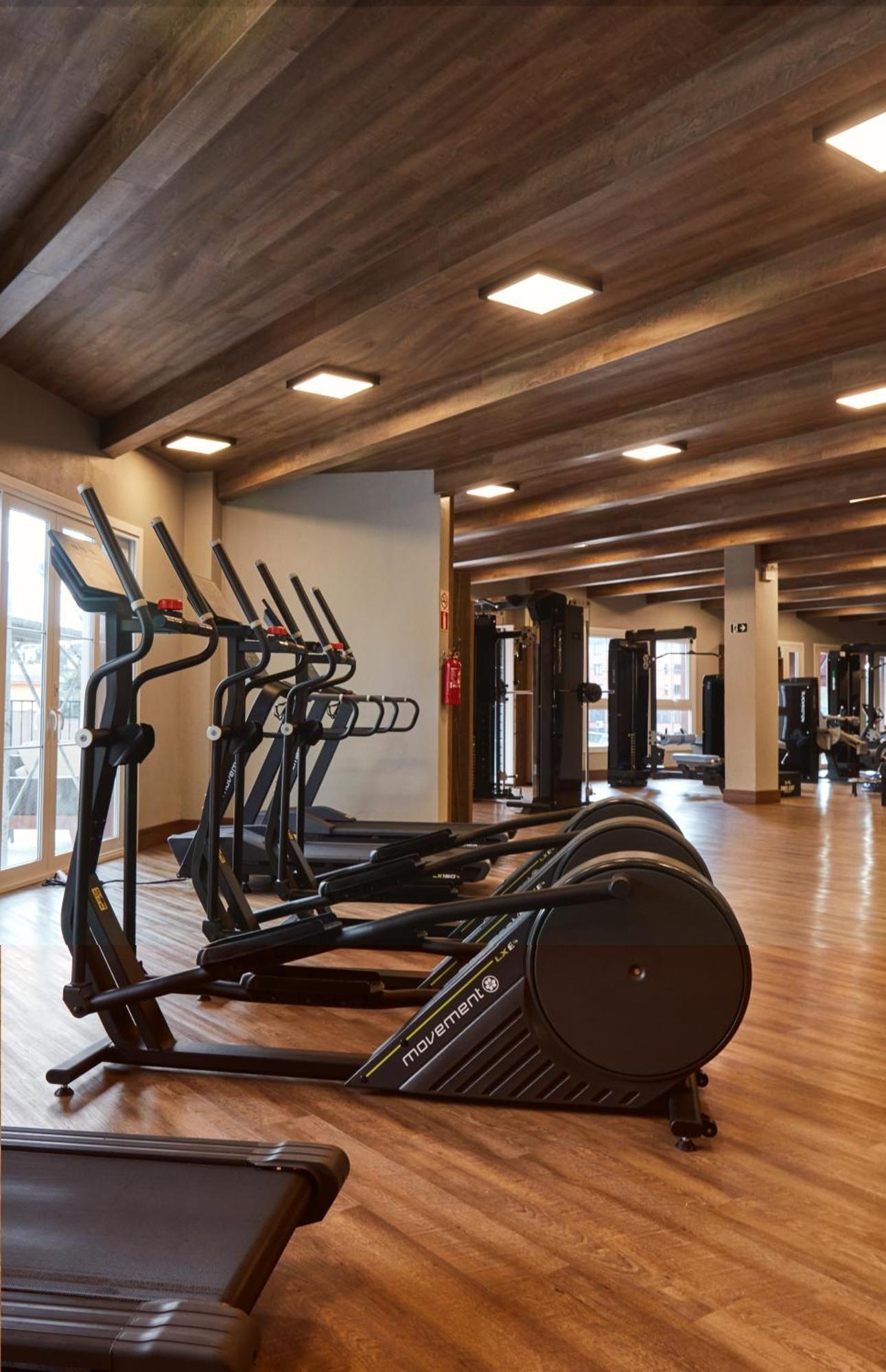 Hotel Buona Vitta Gramado by Gramado Parks Esterno foto The photo shows a modern gym interior with wooden flooring and a ceiling with wooden beams. There are several exercise machines, including elliptical trainers and a treadmill, positioned in the foreground. In the background, there are additional work