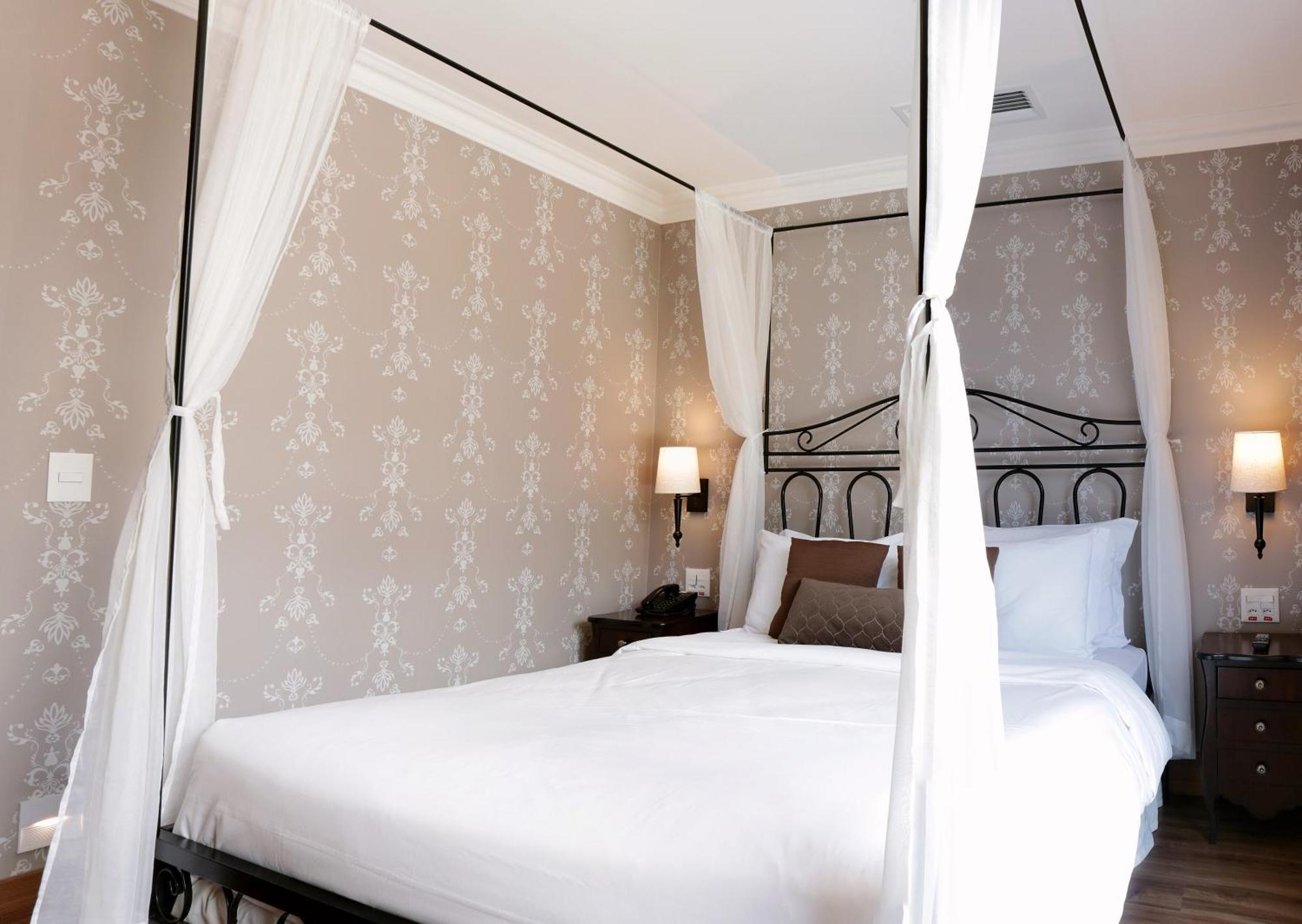 Hotel Buona Vitta Gramado by Gramado Parks Esterno foto The photo shows a elegantly decorated bedroom featuring a four-poster bed with white drapes. The bed is made with white linens and has some brown accent pillows. The walls are adorned with a subtle floral pattern, and there are two bedside lamps prov