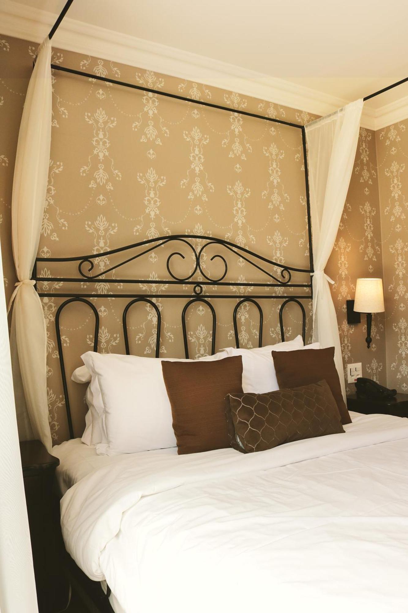 Hotel Buona Vitta Gramado by Gramado Parks Esterno foto The photo shows a cozy bedroom setup featuring a decorative metal bed frame with a scroll design as the headboard. The bed is adorned with several white pillows and two brown decorative cushions. The wall behind the bed is covered with a light-colore
