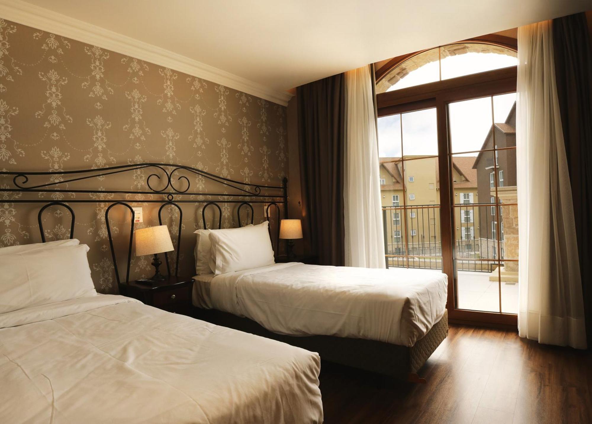 Hotel Buona Vitta Gramado by Gramado Parks Esterno foto The photo shows a well-decorated hotel room featuring two beds. One bed is larger, likely a double bed, while the other is a single bed. The walls are adorned with a floral pattern, and there are bedside lamps next to the larger bed. Large windows wi