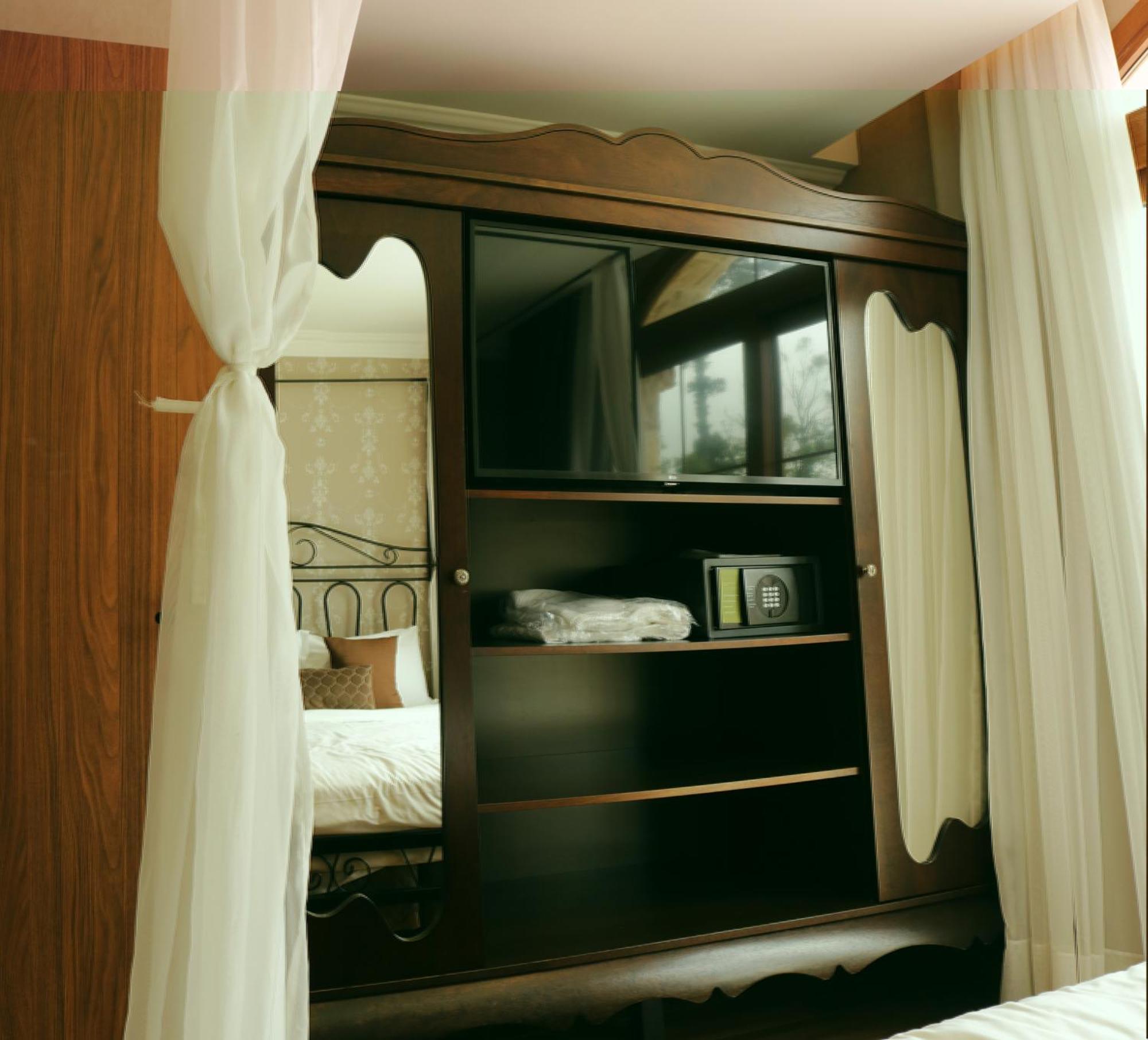 Hotel Buona Vitta Gramado by Gramado Parks Esterno foto The image shows a wooden cabinet with a television mounted on the front. The cabinet has decorative edges and is paired with sheer white curtains on either side. Inside the cabinet, there are shelves, and a small safe or storage box is visible on one