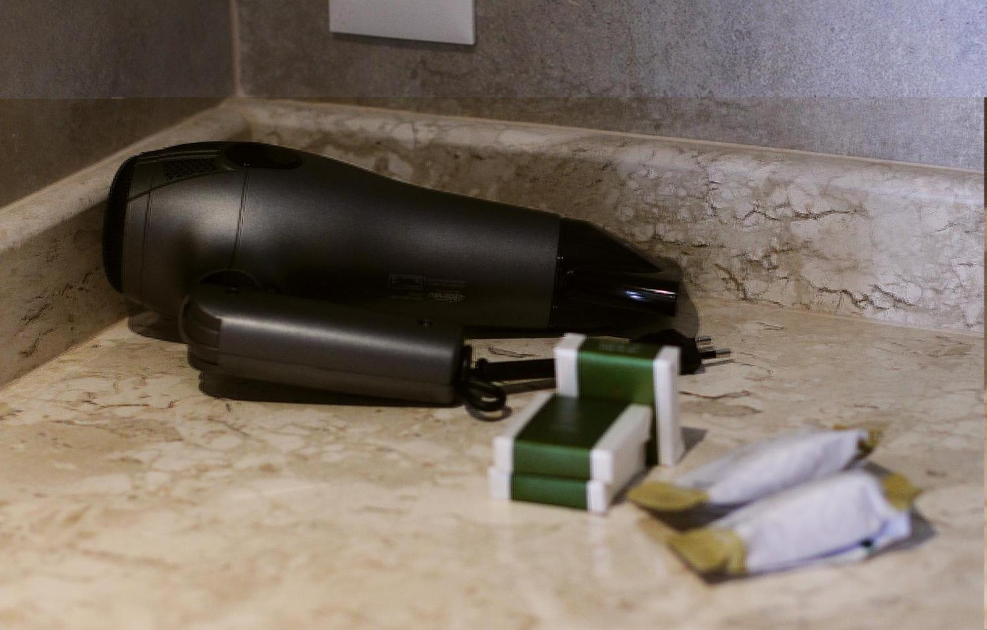 Hotel Buona Vitta Gramado by Gramado Parks Esterno foto The photo shows a black hairdryer placed on a marble countertop. Next to the hairdryer, there are two wrapped items, likely toiletries, with green and white packaging. Additionally, there are two more items, also wrapped, which appear to be in simila