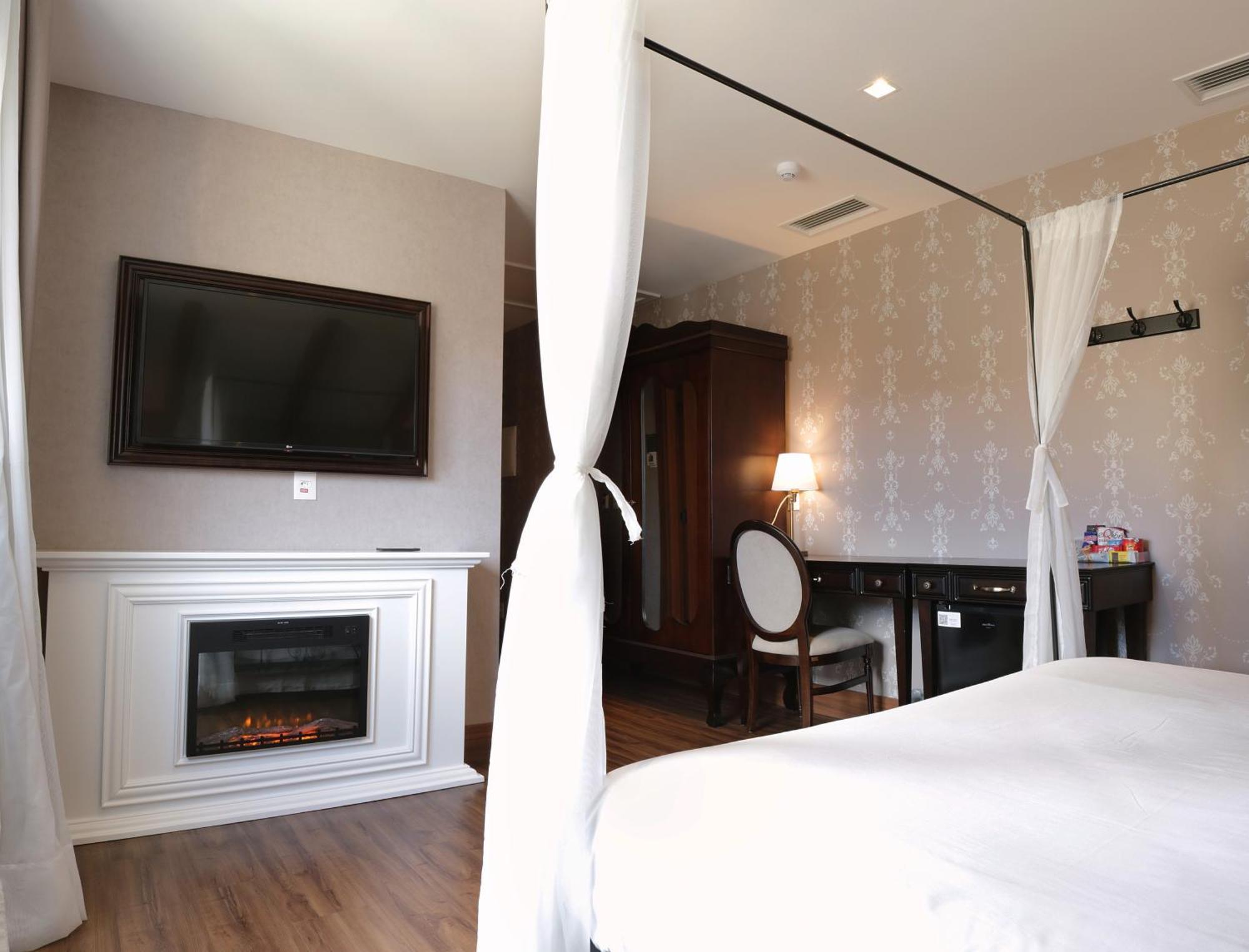 Hotel Buona Vitta Gramado by Gramado Parks Esterno foto The photo shows a cozy hotel room with elegant decor. There is a white bed with a canopy, and a modern television mounted on the wall across from it. To the side, a fireplace is built into a white mantel, adding a warm touch to the space. There's a w