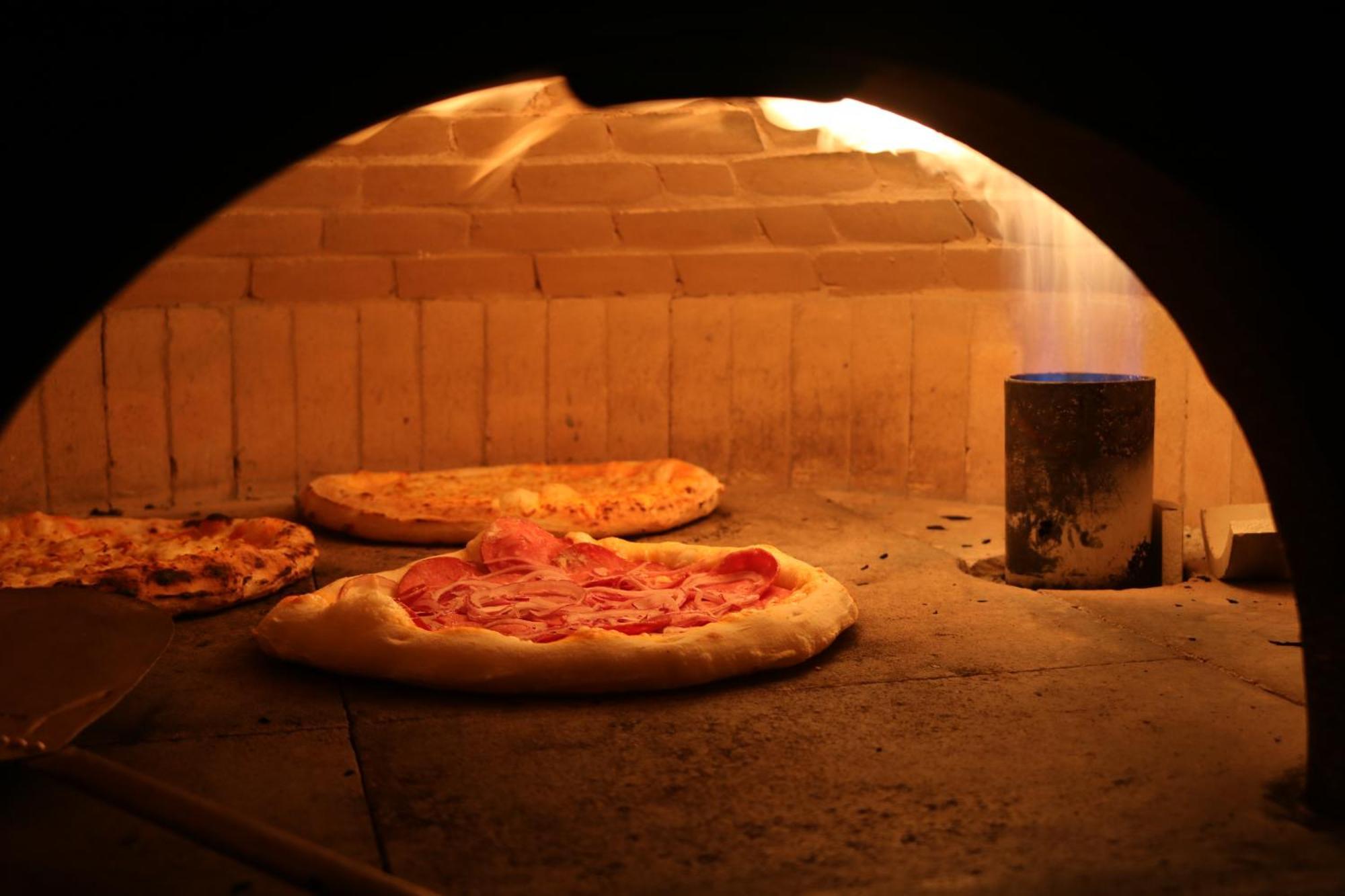 Hotel Buona Vitta Gramado by Gramado Parks Esterno foto The photo shows a traditional pizza oven. Inside the oven, there are several pizzas placed on the stone surface. The pizzas appear to have various toppings, including what looks like cheese and possibly pepperoni. The oven has a warm, glowing ambianc