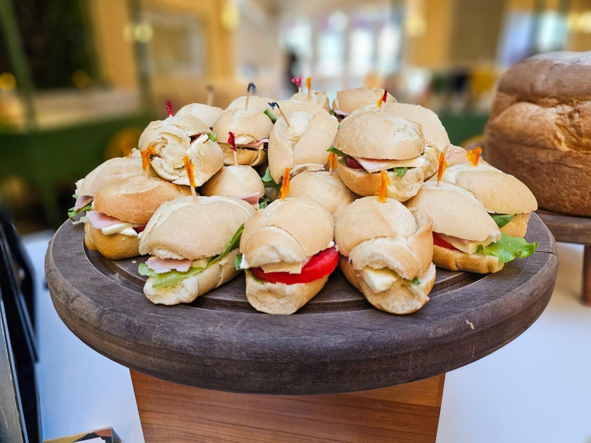 Hotel Buona Vitta Gramado by Gramado Parks Esterno foto The photo shows a platter of small sandwiches, likely sliders, arranged neatly on a wooden serving tray. These sandwiches have various fillings, including what appears to be ham, lettuce, and tomato. They are garnished with colorful toothpicks, and t